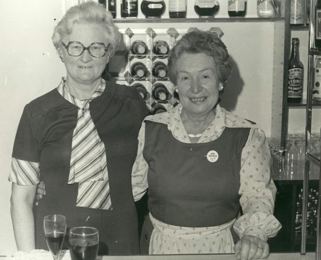 Connie Beak (S.M.) with May Gray (waitress) Serving behind the bar at a retirement party. | JLP Archive Collection